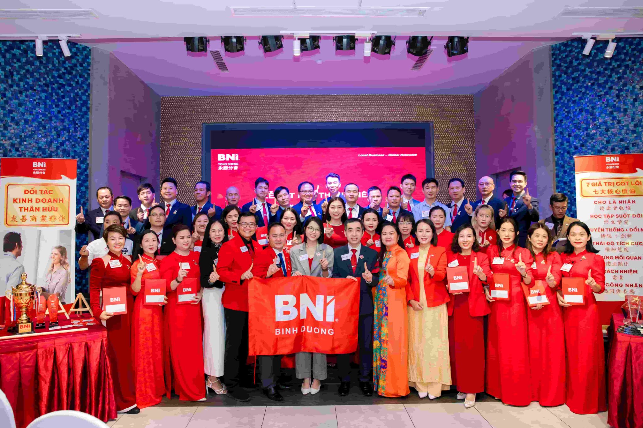 越南BNI永勝分會全體創始會員身著代表專業與熱情的紅色及深色正裝，自信比出「第一」手勢。在「挑戰無限（Thách thức mọi giới hạn）」的口號引領下，這群來自平陽各產業的菁英展現出高昂士氣，誓言透過 BNI 系統共創商業高峰。（圖／欒金鳳 提供）